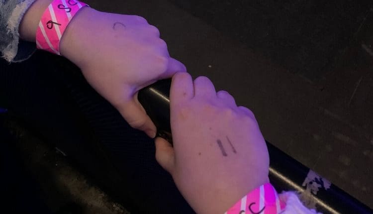 Two fans holding the barricade with their line number on their hands and wristbands.