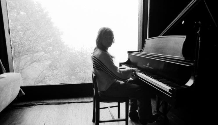 Photo of Clairo sitting by the piano for her album Sling