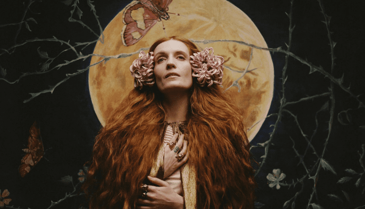 Album cover for Dance Fever. Florence Welch is wearing a dark colored cloak, her hair is down and is adorned with two pink flowers on both sides of her head. Her hands are reaching up to her neck.
