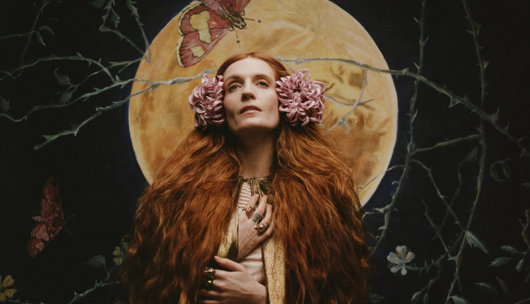 Album cover for Dance Fever. Florence Welch is wearing a dark colored cloak, her hair is down and is adorned with two pink flowers on both sides of her head. Her hands are reaching up to her neck.