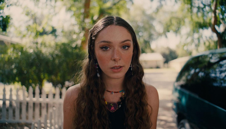 Holly Humberstone is looking directly at the camera, her hair is down and is wavy. She is wearing a black tank top and black matching choker necklace.