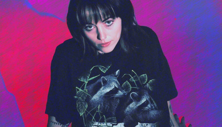 Sasha Alex Sloan is moodily looking at the camera, wearing a black shirt and edited in front a bright purple and pink background