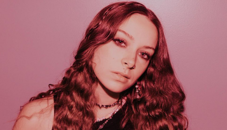 holly humberstone looks directly in the camera the picture is tinted light pink with hues of black and brown