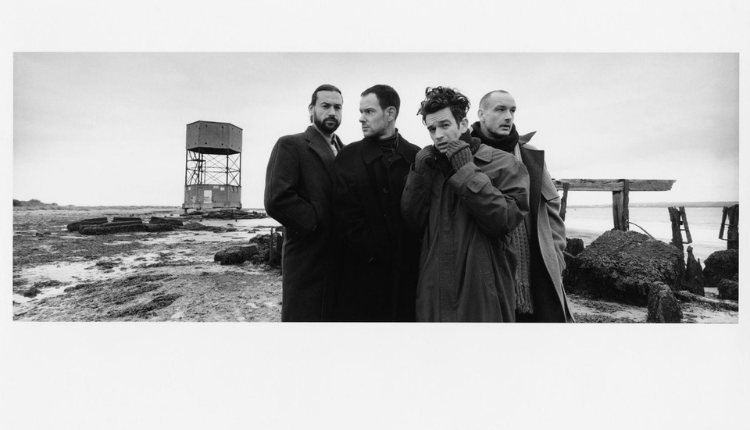 The 1975 are on a beach wearing posh clothes